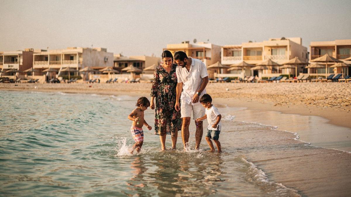 Two parents and two children paddling at the shoreline of a shallow Red Sea beach in late afternoon light